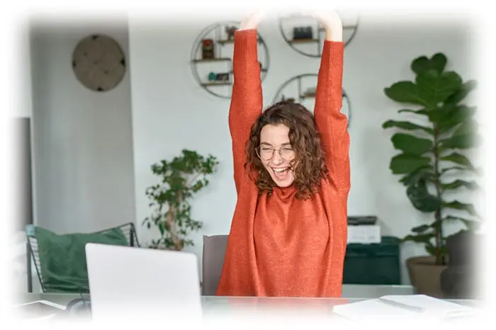A woman is raising her arms in front of a laptop.